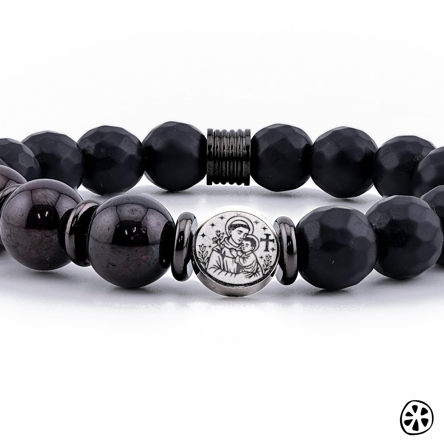 Close-up detail photo of a handmade St. Anthony of Padua bracelet featuring 10mm Black Faceted Onyx and deep Garnet gemstone beads. The stainless steel double-sided St. Anthony medal is centered between polished spacers, highlighting its engraved depiction of the saint with the Child Jesus. Displayed on a clean white background, this Catholic protection bracelet shows premium craftsmanship and elegant spiritual design.