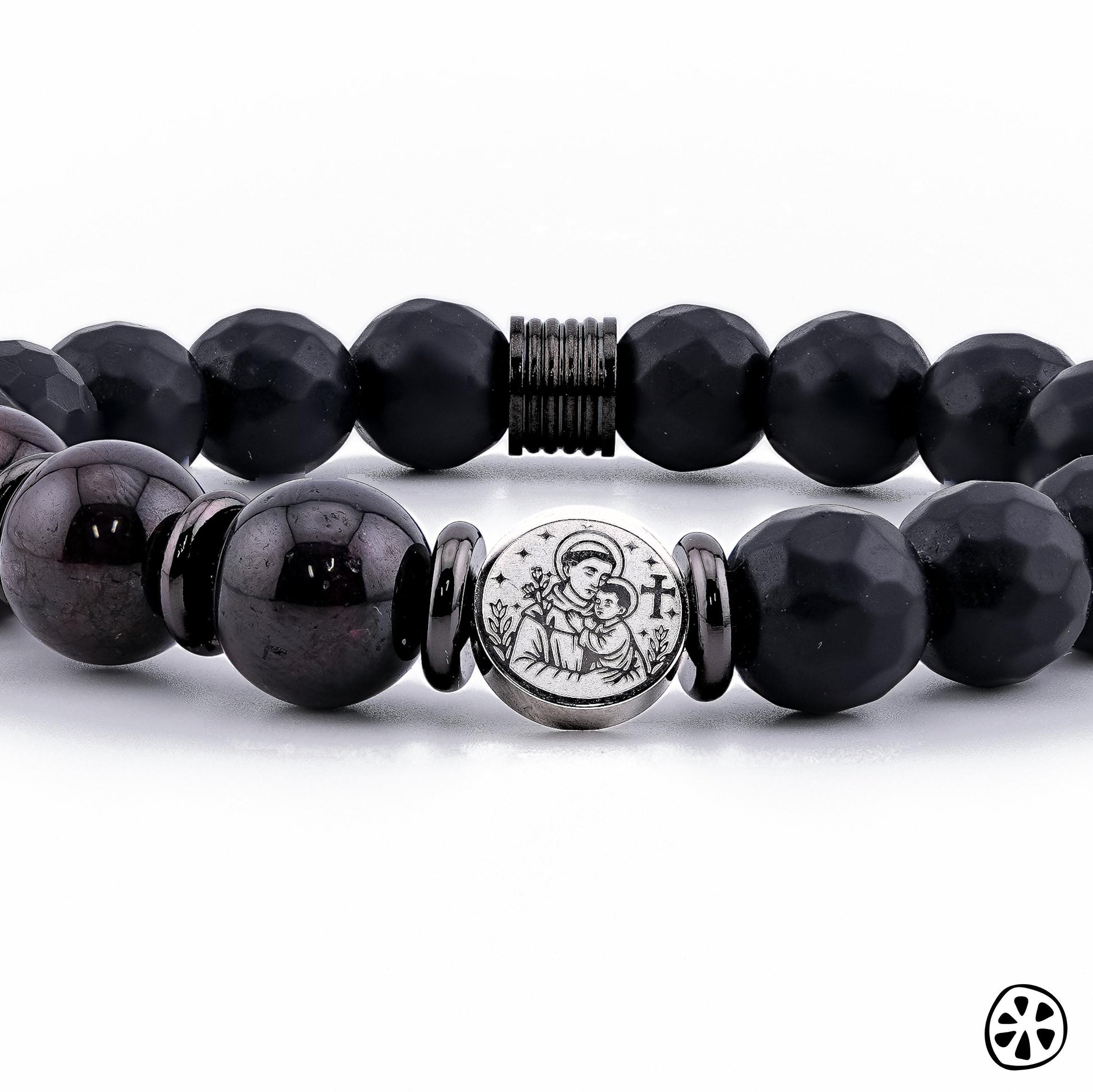 Close-up detail photo of a handmade St. Anthony of Padua bracelet featuring 10mm Black Faceted Onyx and deep Garnet gemstone beads. The stainless steel double-sided St. Anthony medal is centered between polished spacers, highlighting its engraved depiction of the saint with the Child Jesus. Displayed on a clean white background, this Catholic protection bracelet shows premium craftsmanship and elegant spiritual design.