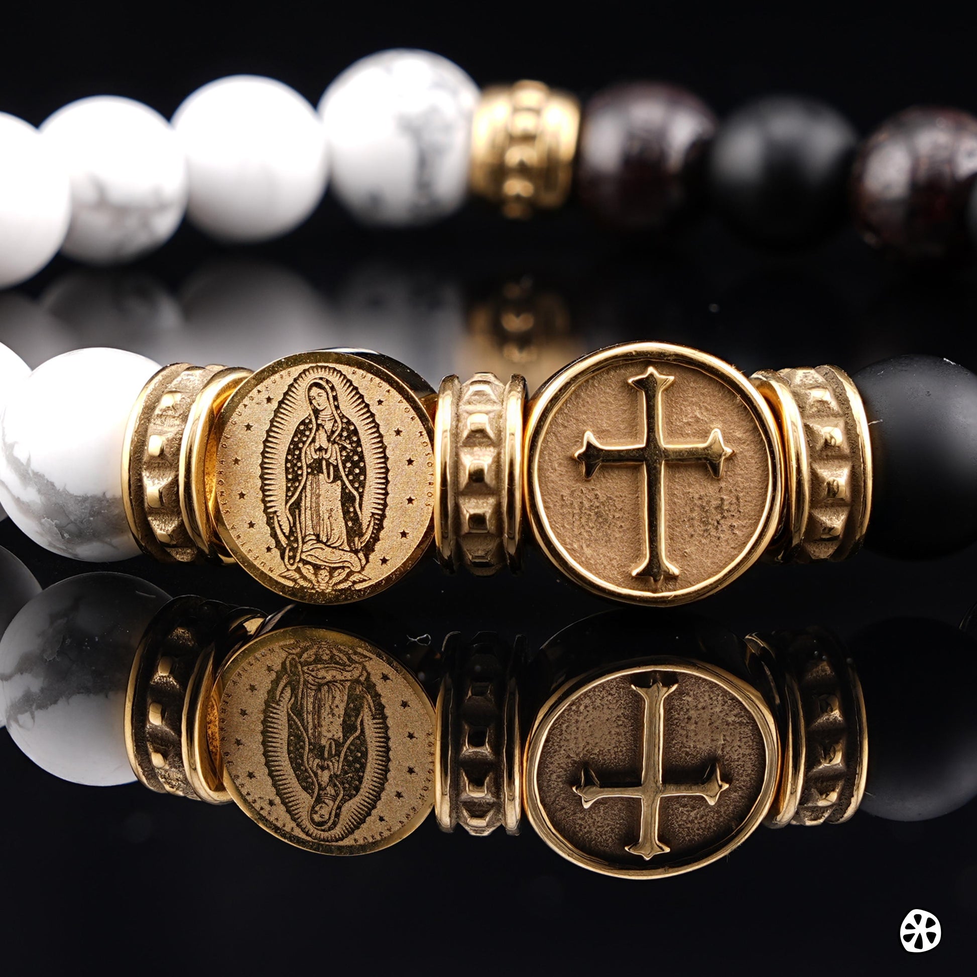 Close-up of Our Lady of Guadalupe bracelet featuring gold-tone Guadalupe medal and cross charm, accented with 18K gold PVD stainless steel spacers. Set with frosted white howlite, black onyx, and polished red garnet beads. Handmade Catholic jewelry for men and unisex wear, highlighting fine engraving details and premium materials. Faith-inspired bracelet ideal for prayer, daily wear, or gifting for baptism, confirmation, and religious occasions.