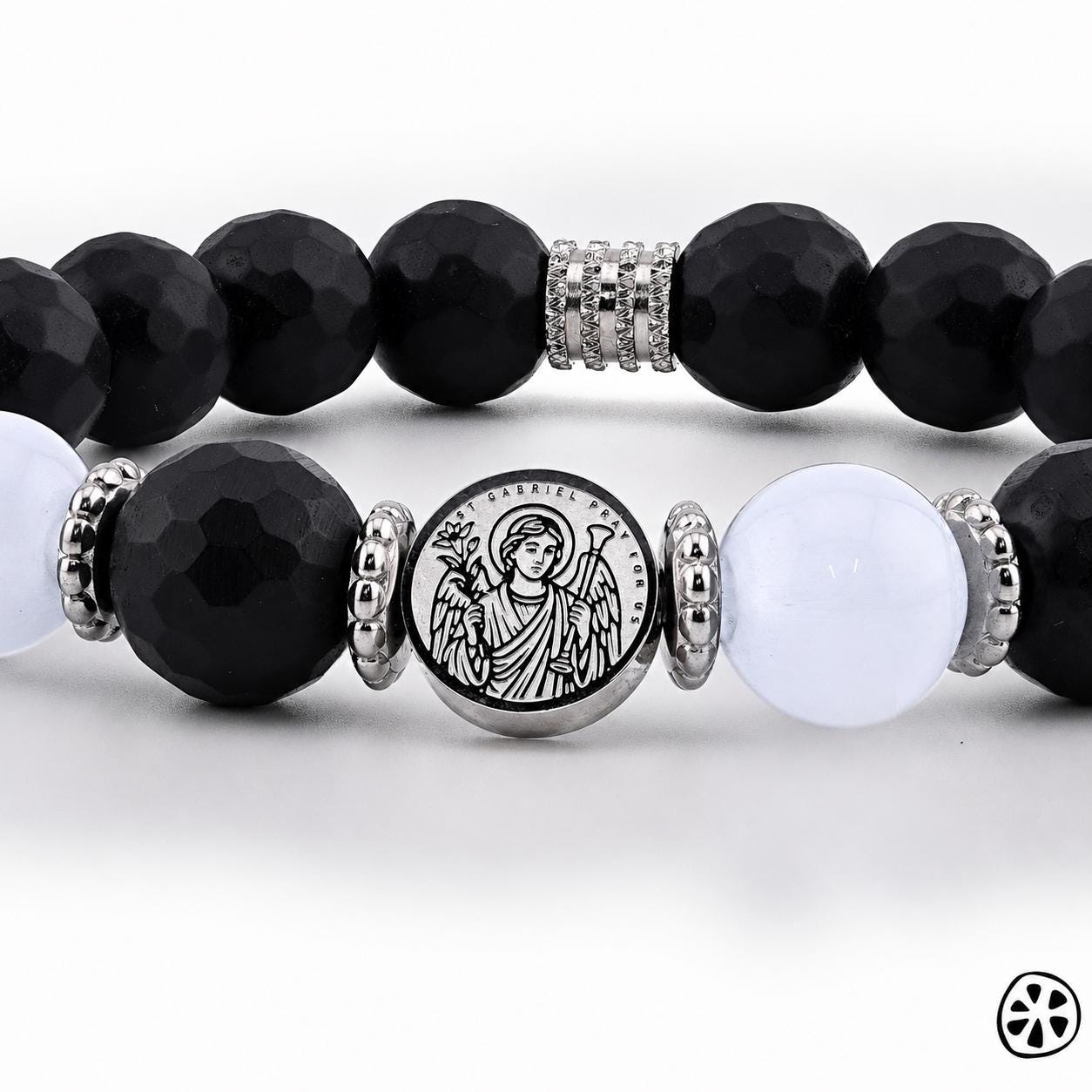 Close-up front view of a beaded bracelet featuring faceted black onyx beads, smooth white selenite beads, and stainless steel spacers. Centered in the design is a round stainless steel charm engraved with Archangel Gabriel holding symbolic elements, surrounded by his sigil. The photo highlights bead texture, polished metal details, and the engraved artwork against a clean white background.
