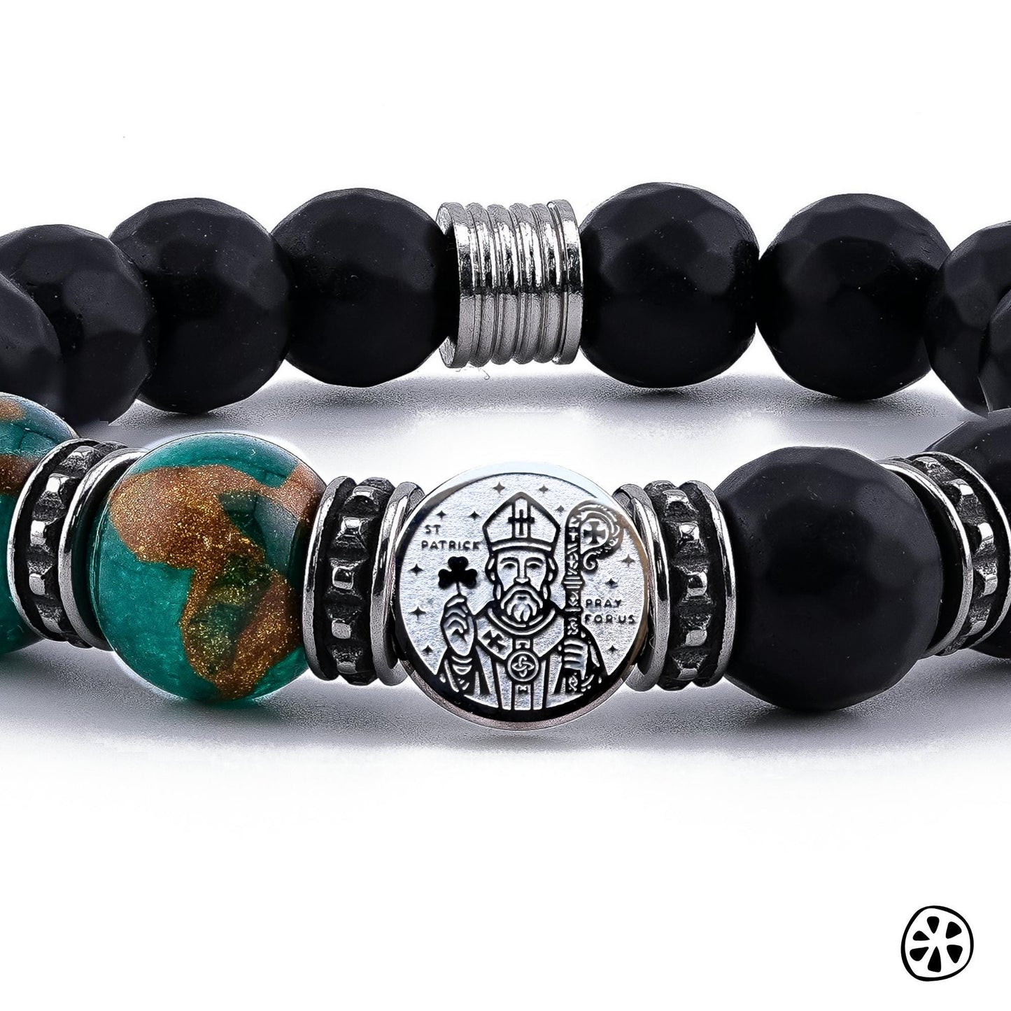 Close-up photo of the handmade St. Patrick Protection Bracelet showing detailed 10mm green cloisonné beads with brown and gold enamel accents, black faceted matte onyx beads, and a dual-sided stainless steel St. Patrick medal. The image highlights the engraved saint design, the tarnish-free stainless steel spacers, and the rich texture and color contrast of the premium beads in sharp focus.