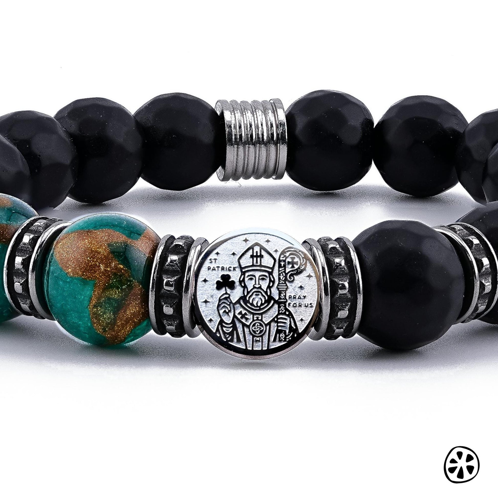 Close-up photo of the handmade St. Patrick Protection Bracelet showing detailed 10mm green cloisonné beads with brown and gold enamel accents, black faceted matte onyx beads, and a dual-sided stainless steel St. Patrick medal. The image highlights the engraved saint design, the tarnish-free stainless steel spacers, and the rich texture and color contrast of the premium beads in sharp focus.